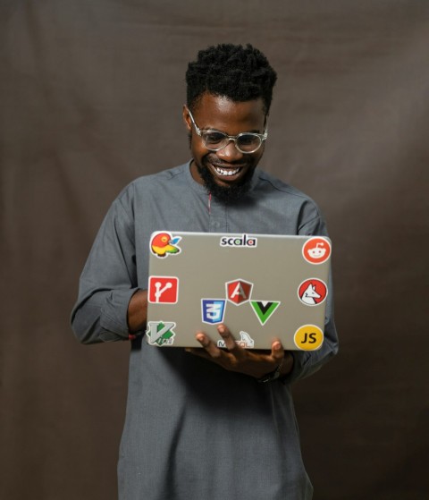 a man holding a laptop with a lot of stickers on it