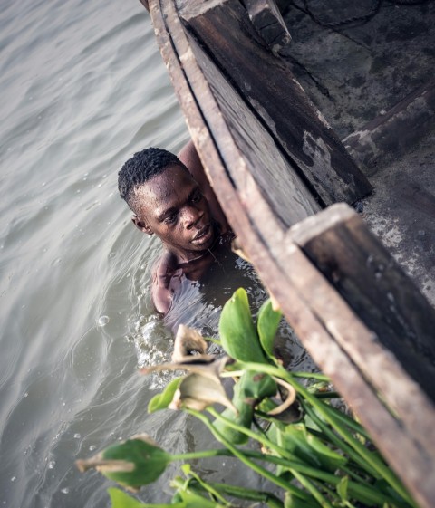 man in body of water holding on side of boat