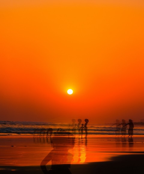 a group of people standing on top of a beach under a sunset