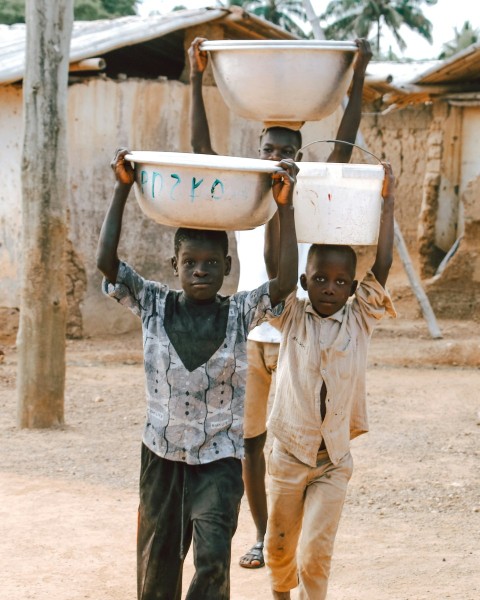 two young boys carrying bowls on their heads