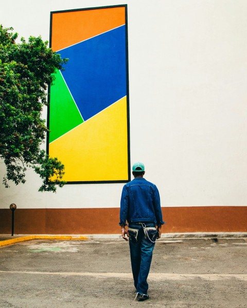 a man walking down a street past a large painting