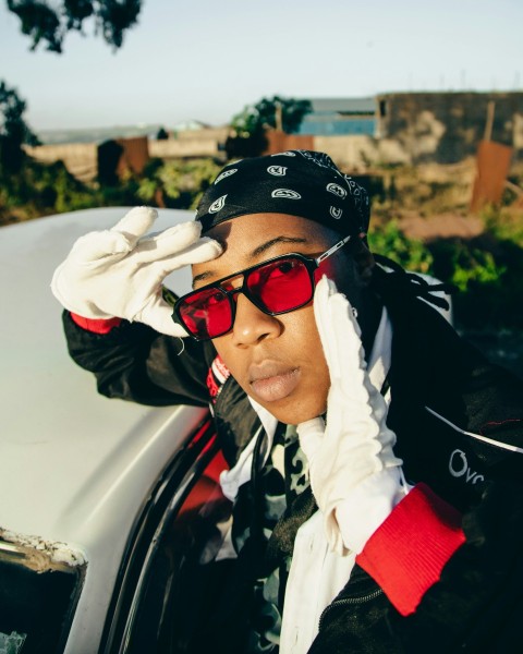 a man in sunglasses and a hat leaning on a car