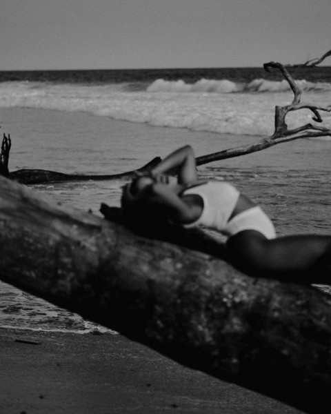 a black and white photo of a woman laying on a log Klxy