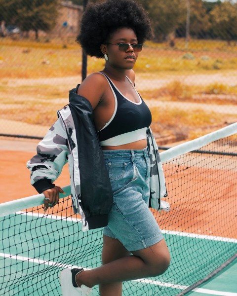 woman in blue denim jacket and blue denim shorts standing beside white net during daytime