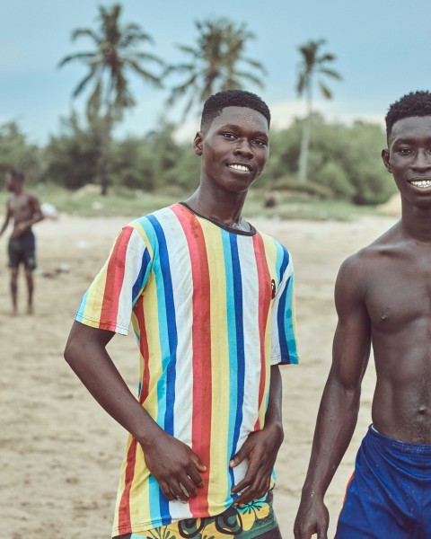 man in blue shorts standing beside man in white orange and blue stripe shirt