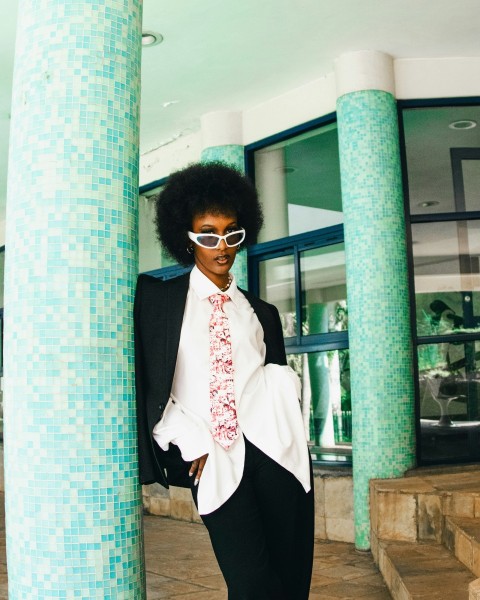 a woman in a suit and sunglasses leaning against a column