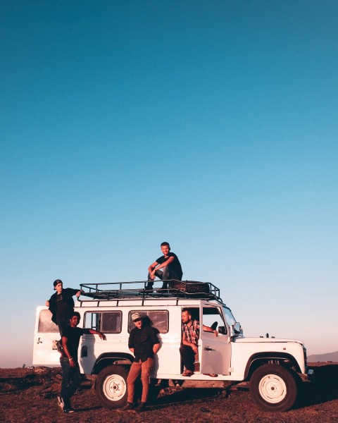 man in red shirt sitting on white suv during daytime