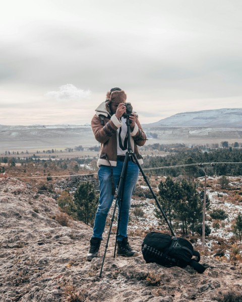 woman in brown jacket and blue denim jeans standing on brown rock formation during daytime