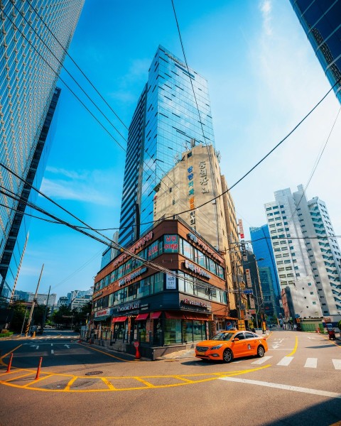 a yellow car driving down a street next to tall buildings