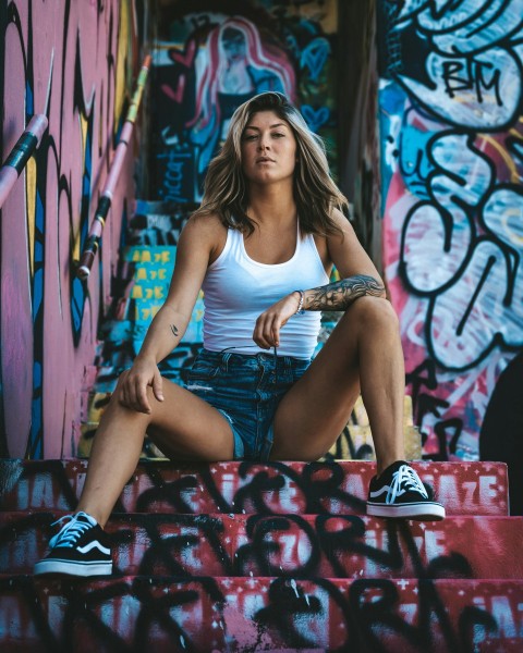 woman in white tank top and blue denim shorts sitting on red and white floral textile WH