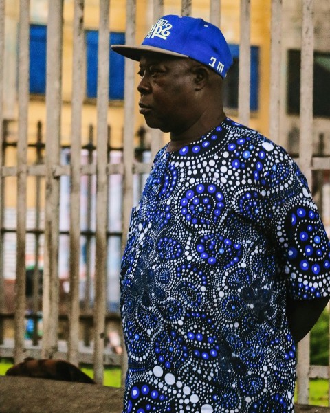 man in blue and white floral shirt wearing blue cap standing near brown metal fence during