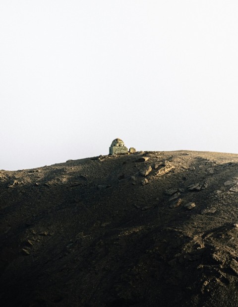 a lone sheep standing on top of a rocky hill