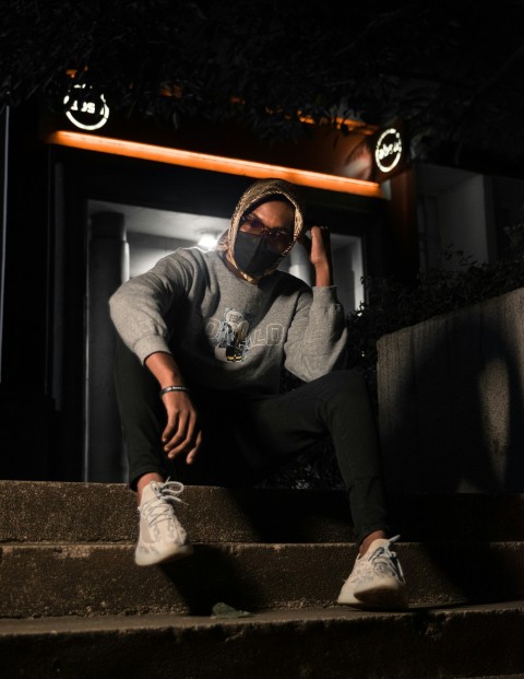 man in gray long sleeve shirt and black pants wearing black and white face mask sitting