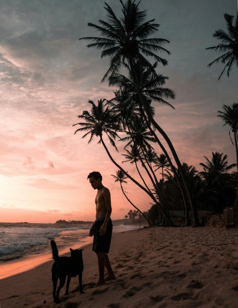 topless man standing near dog beside seashore