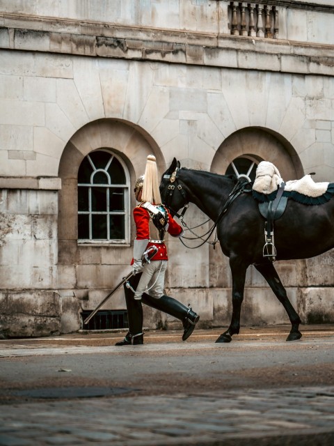 a man in uniform walking a horse down the street