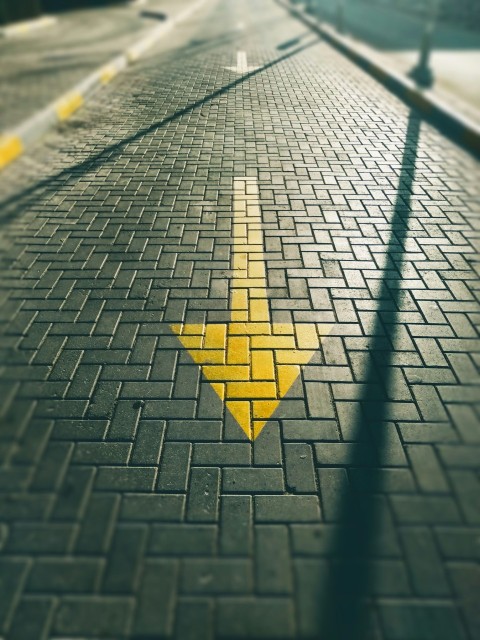 a yellow arrow painted on a brick road