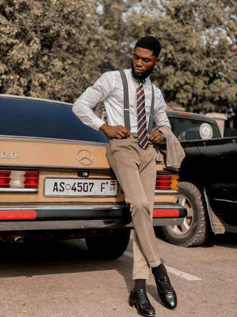 a man in a suit and tie leaning against a car