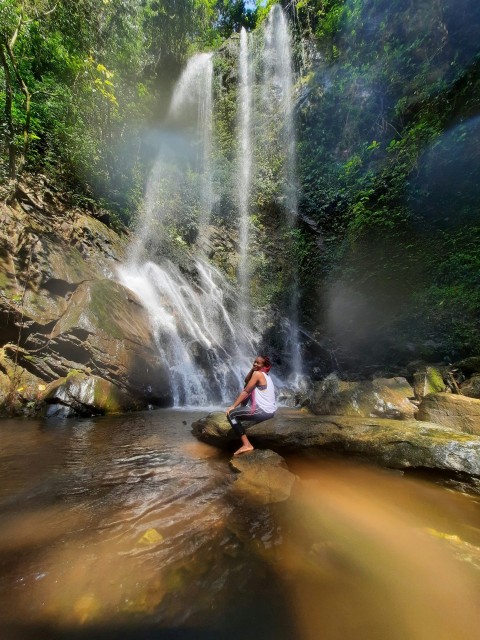 woman in white shirt and black pants standing on brown rock near waterfalls during daytime