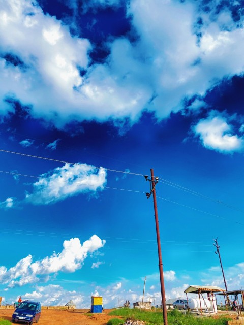 a car driving down a dirt road under a cloudy blue sky