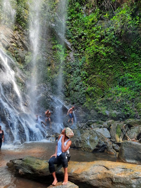 woman in black tank top and black shorts sitting on rock near waterfalls during daytime