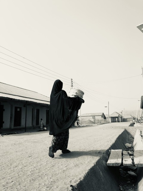 a woman walking down a street carrying a basket on her head