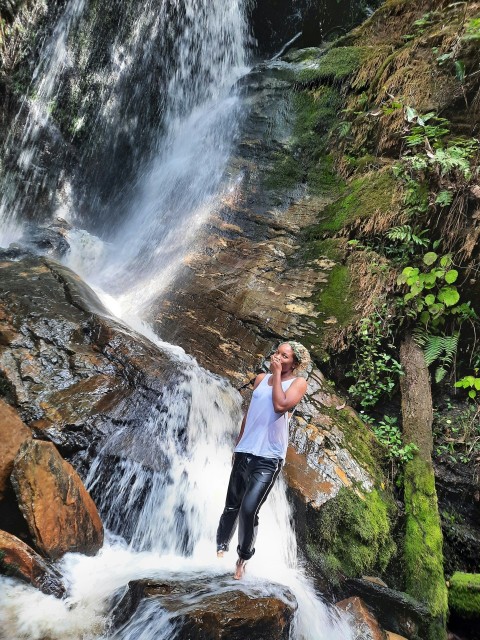 woman in black tank top and black pants standing on rock near waterfalls during daytime