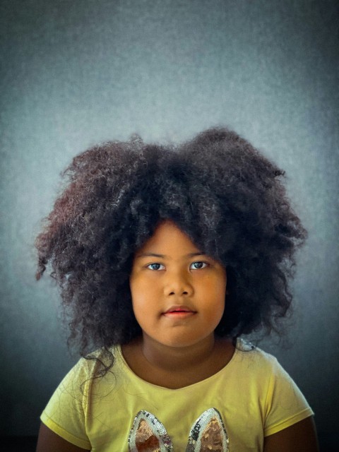 a little girl with a big afro standing in front of a wall