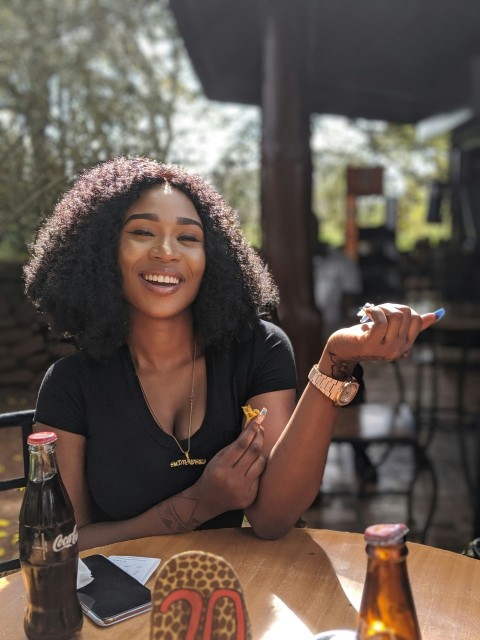 smiling woman wearing black scoop neck top sitting in front of brown wooden table