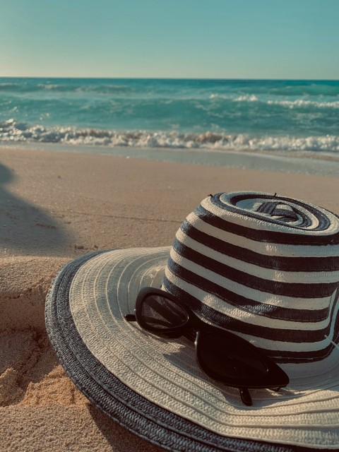 brown and white fedora hat on brown sand near sea during daytime e