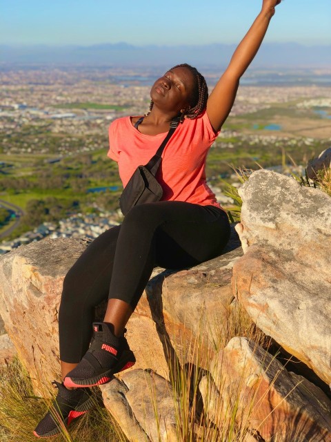 woman in orange shirt and black pants sitting on rock during daytime