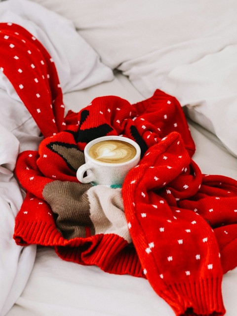 round white ceramic mug with coffee beverage inside on top of red and white polka dot knitted sweater N4_O3dYOP