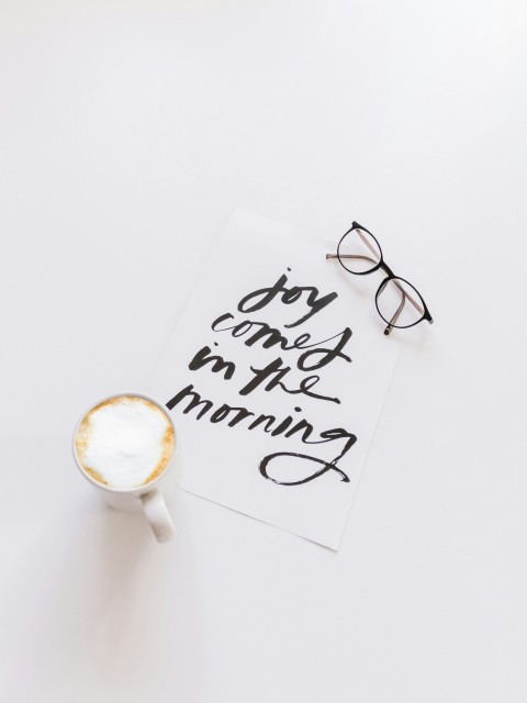 black framed eyeglasses beside white ceramic coffee cup