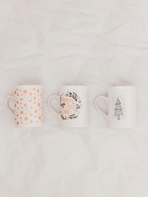 three white and multicolored ceramic mugs on white textile Wasu92