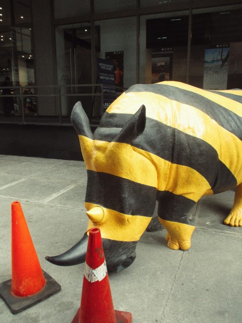 a yellow and black rhino statue next to a traffic cone