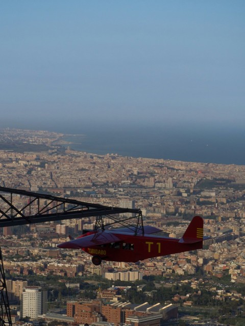 a red and yellow plane flying over a city f0YuO6dW