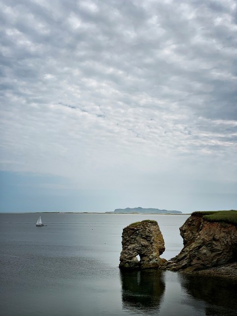 a sailboat is in the water near a rock outcropping