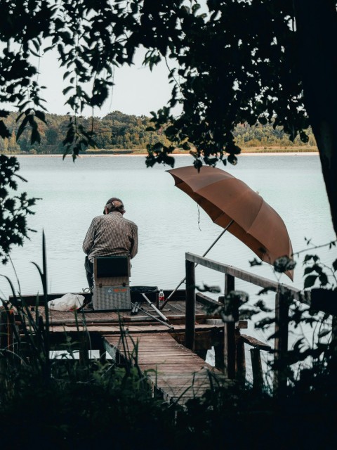 man in gray shirt sitting on brown wooden bench near body of water during daytime