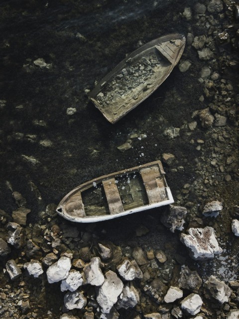 two small boats sitting on top of a rocky beach