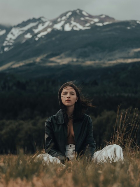 a woman sitting in a field with mountains in the background