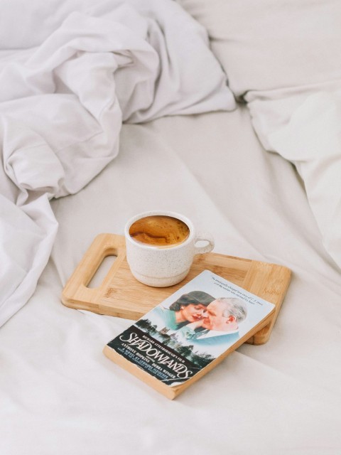 white ceramic mug with coffee on brown wooden serving tray and book TMSQ0Yar7