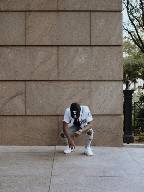 man in black t shirt and white shorts sitting on concrete wall during daytime