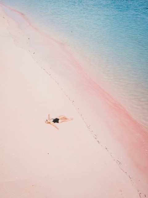 a woman laying on a beach next to a body of water pVXWsb