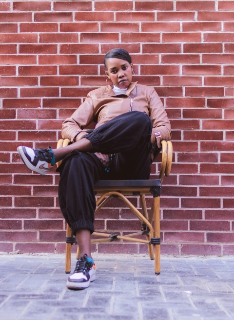 a woman sitting in a chair with a brick wall behind her vKa