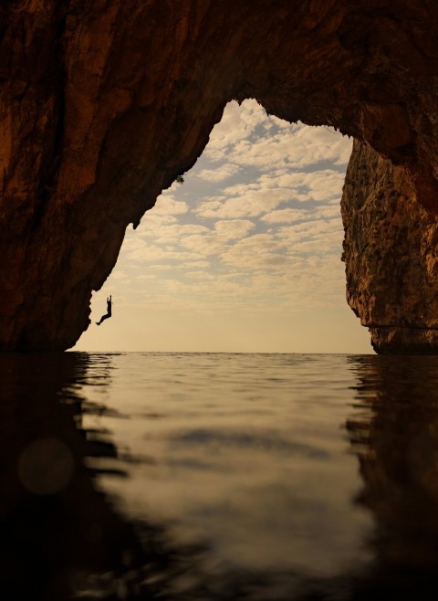 a person standing in the water in front of a cave  YRD4nS0N