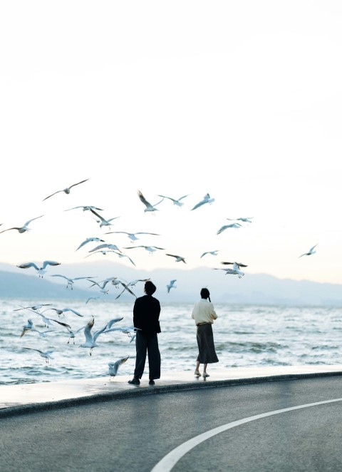 a man and a woman standing on the side of a road near the ocean