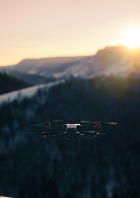 white and black drone flying over the green trees during daytime