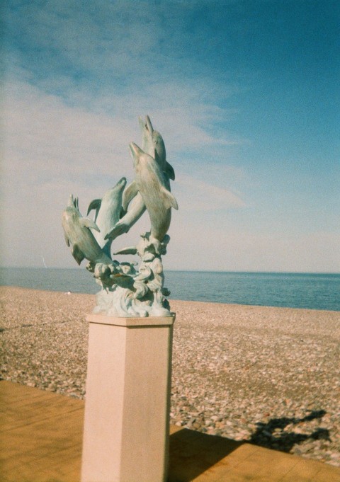 a statue of a bird on a beach next to a body of water