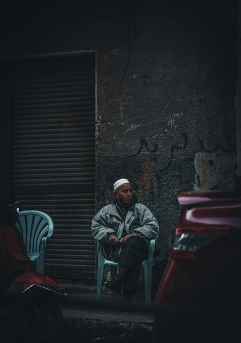 man in gray jacket and black pants sitting on green plastic chair