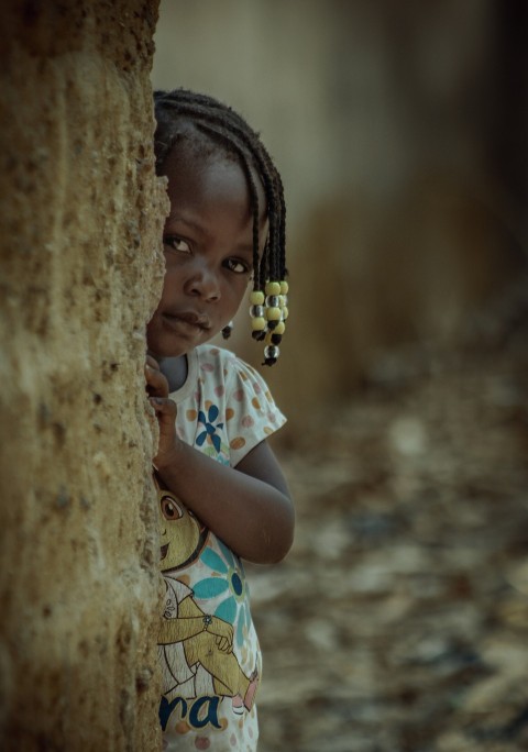 a little girl standing next to a stone wall