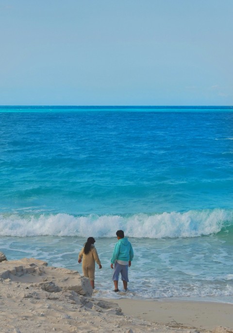 a man and a woman standing on a beach next to the ocean